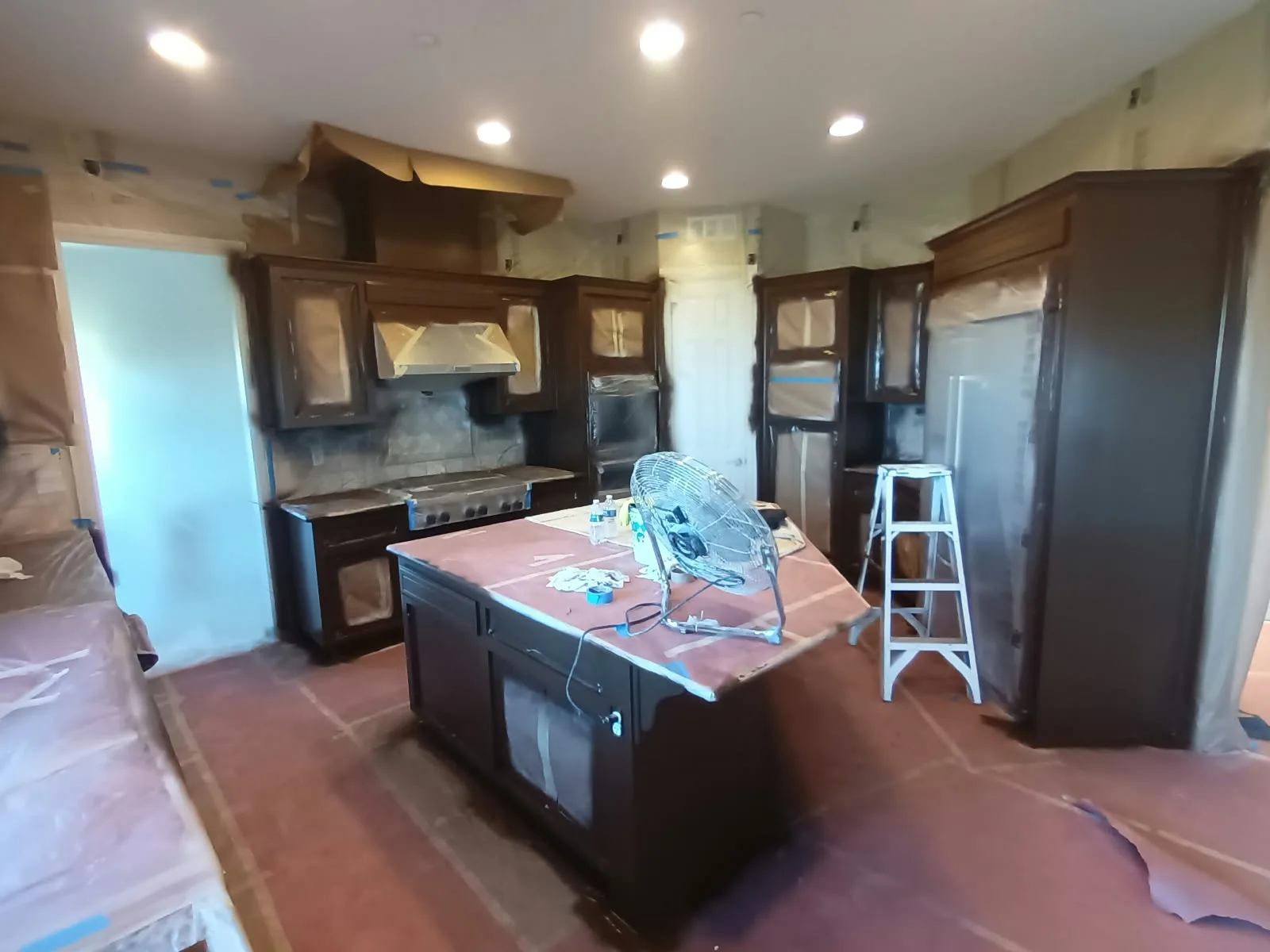 Cabinet refinishing in San Jose, CA: kitchen with covered island and fan running during finishing