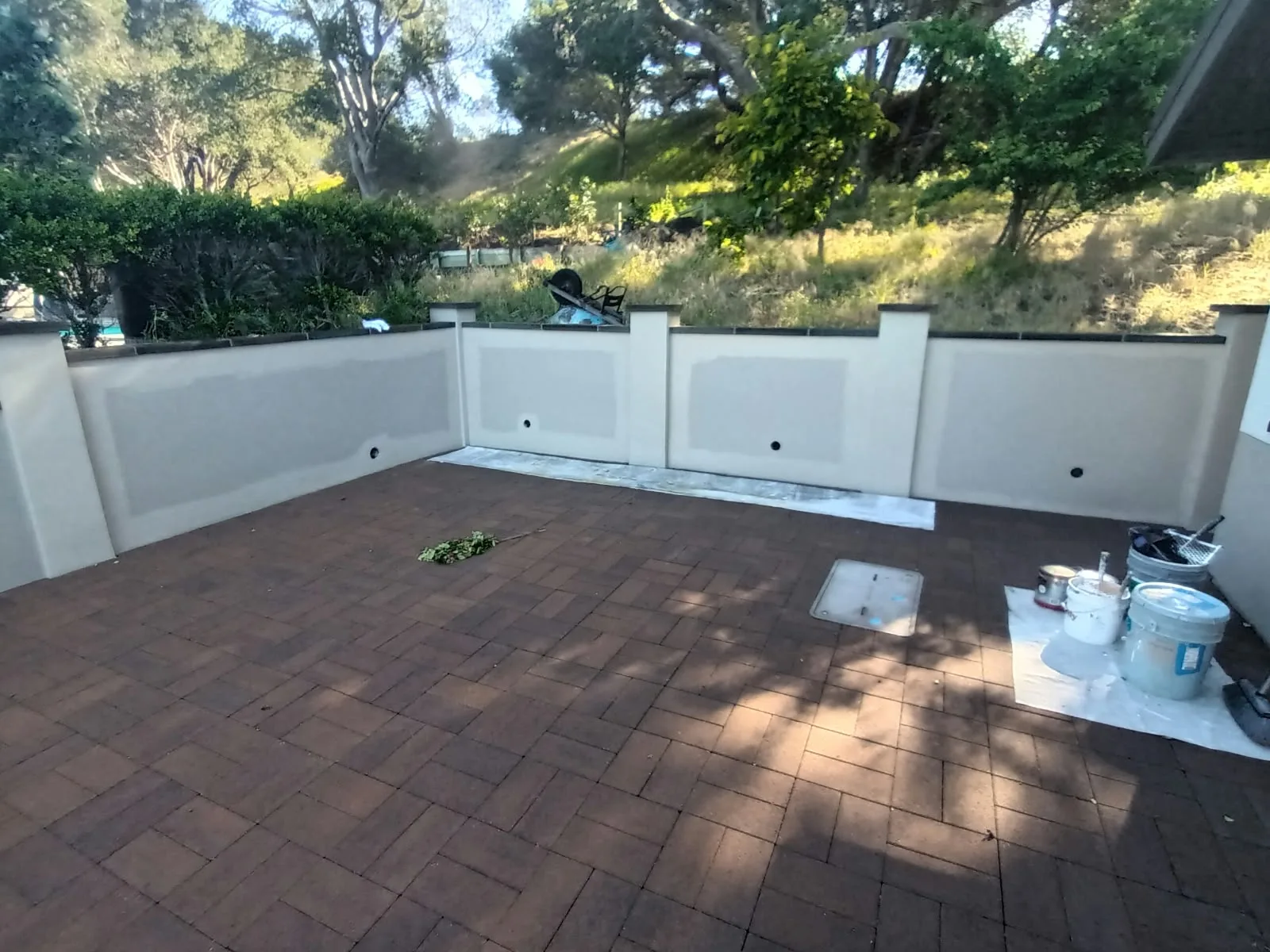 Exterior painting in San Jose, CA: stucco patio wall being painted with paint buckets on site
